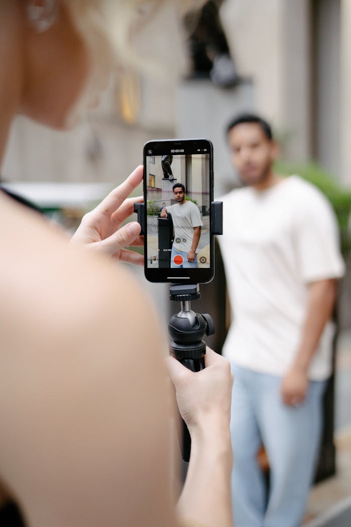 Woman filming a man with a cellphone on a tripod outside, showcasing modern photography.